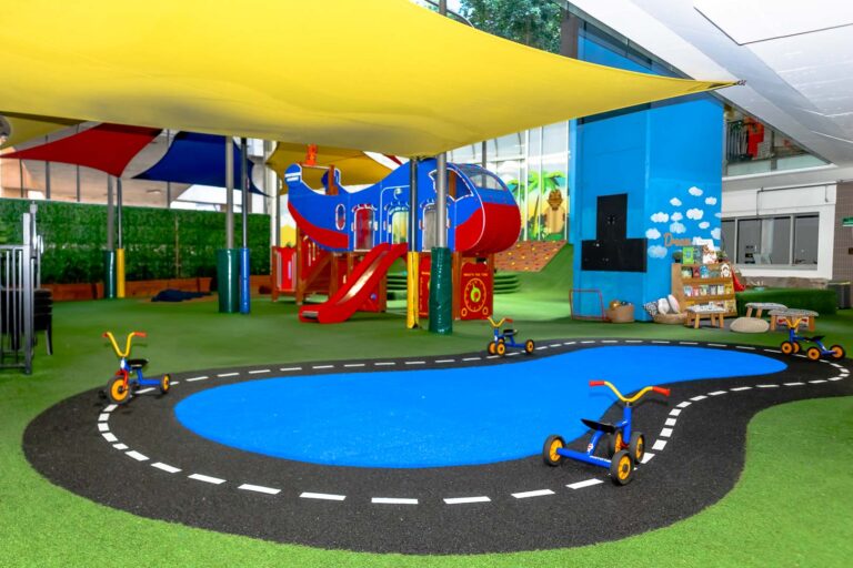 Outdoor playground at Montessori Academy’s Barangaroo childcare, with a pedal kart track, playhouse and turfed play areas.