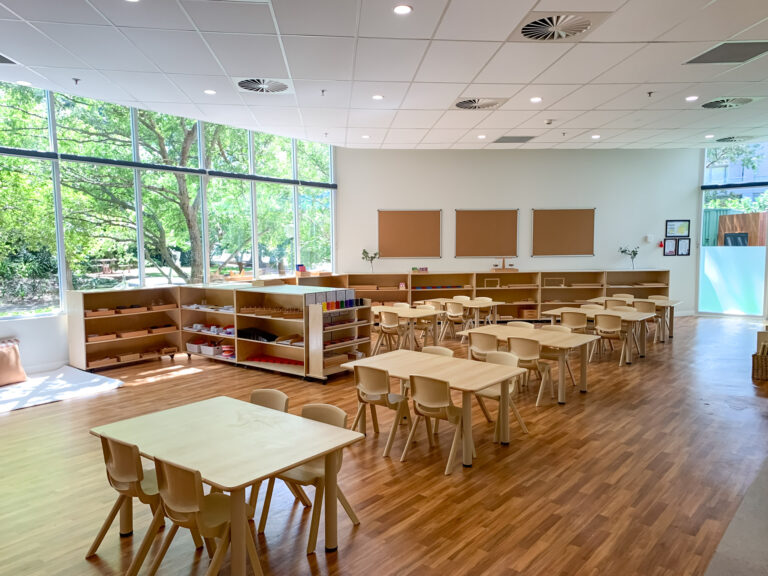 Interior of a classroom at Montessori Academy’s Chatswood Childcare Centre with wooden floors, tables, chairs and shelving.