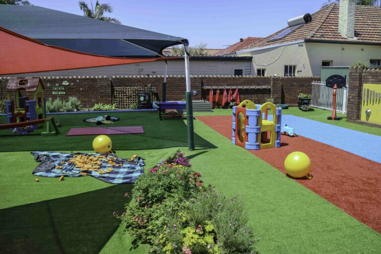 Colourful turfed and sheltered outdoor playground with playhouses at Montessori Academy’s Croydon Childcare Centre.