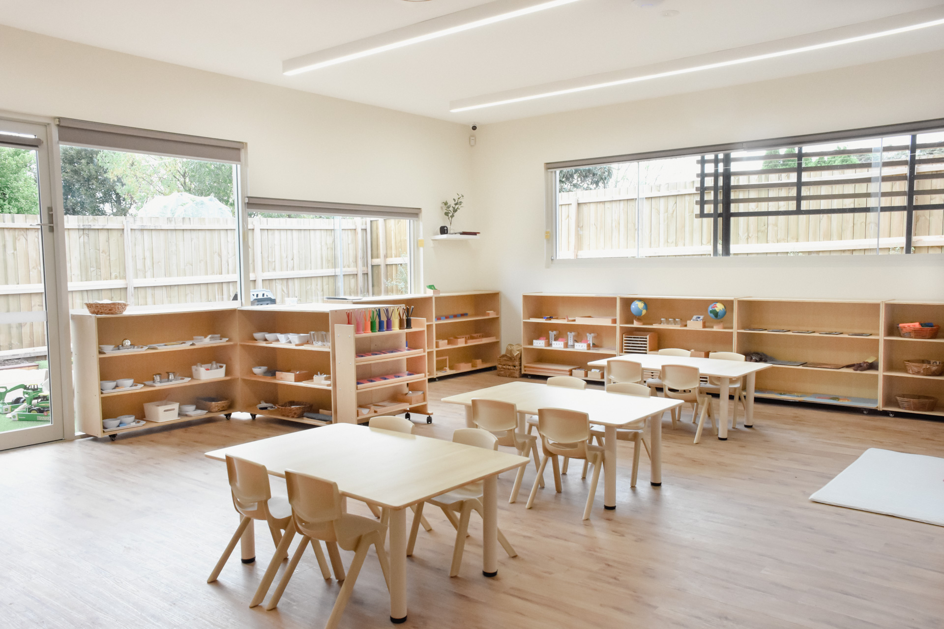 Childcare Montessori Preschool Classroom with open shelving, desks and chairs, and Montessori materials.