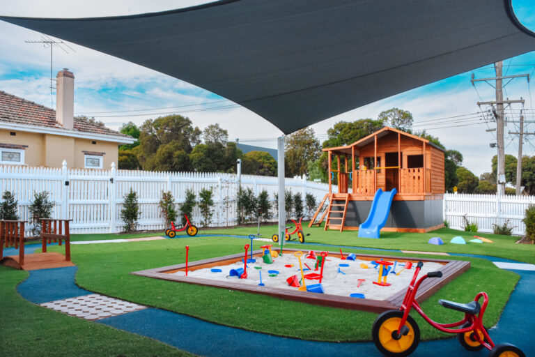 Outdoor playground at Montessori Academy’s Elsternwick daycare centre, with a sand pit, playhouse, slide and bike track.