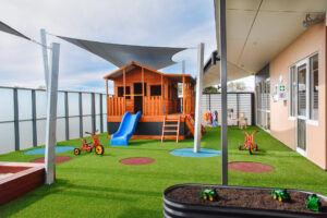 Childcare outdoor playground with cubby house, bikes, and shade sails