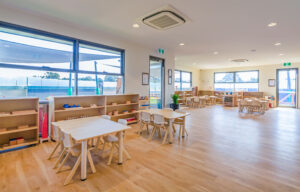 Childcare Montessori Preschool Classroom with open shelving, desks and chairs, and Montessori materials.