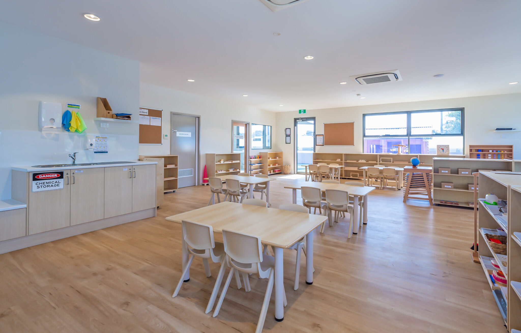 Childcare Montessori Preschool Classroom with open shelving, desks and chairs, and Montessori materials.