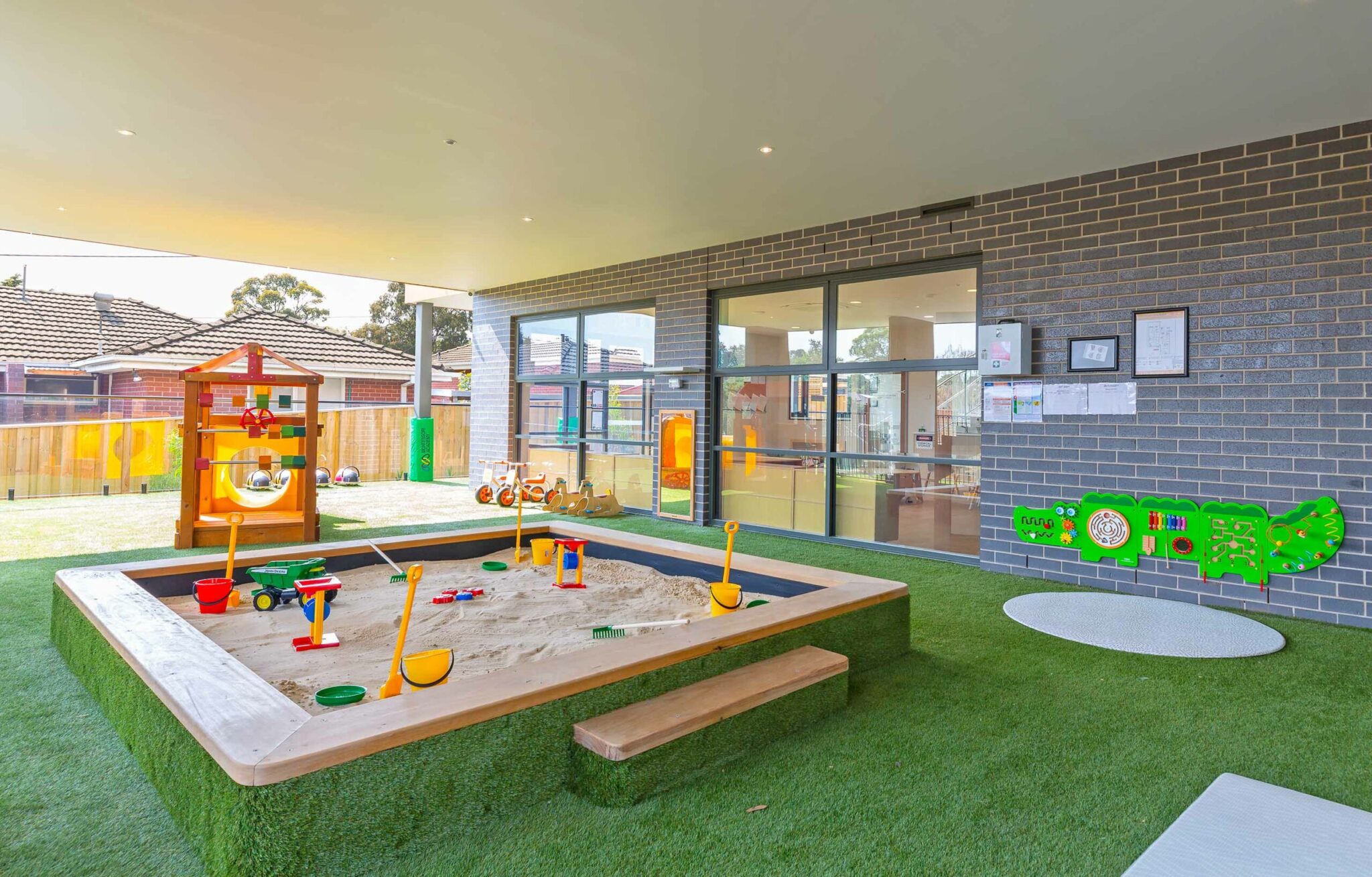 Childcare infant outdoor area with sandpit, sensorial puzzle, and play equipment