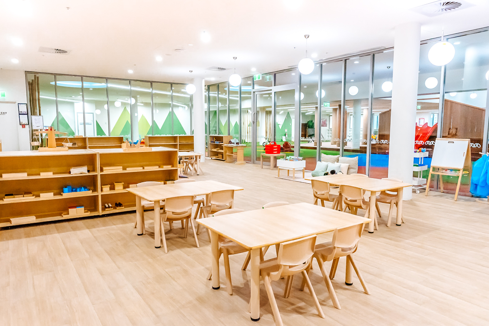 Childcare Montessori Preschool Classroom with open shelving, desks and chairs, and Montessori materials.