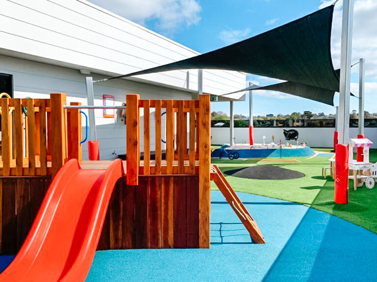 Colourful outdoor playground with a red slide and a sand pit at Montessori Academy’s Box Hill Childcare Centre.