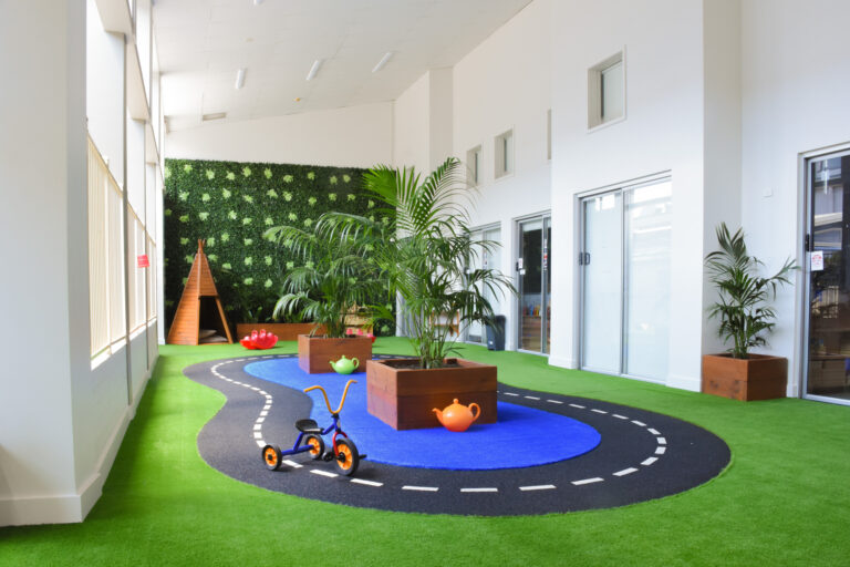 Indoor turfed play area with a pedal kart track and plants at Montessori Academy’s Leichhardt childcare centre.