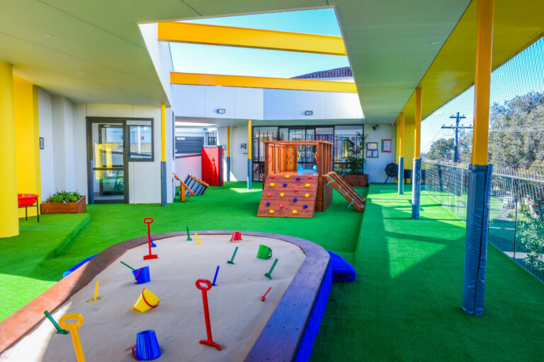 Turfed indoor playground at Montessori Academy’s Belfield childcare, with a sand pit and play house with climbing ramp.