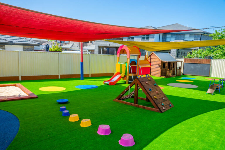 Outdoor playground at Montessori Academy’s Condell Park childcare, with a sandpit, climbing wall and turfed play areas.