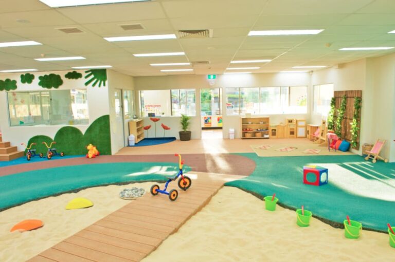 Large indoor play area with sandpit and children’s push bikes at Montessori Academy’s Macquarie Park childcare centre.