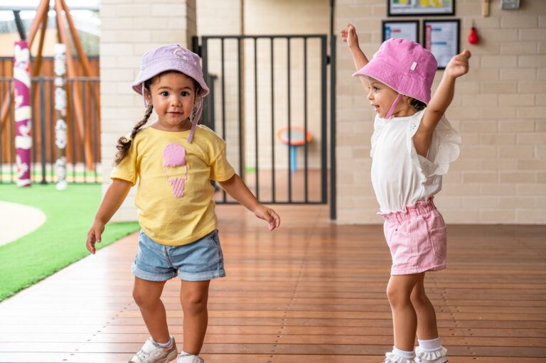 Two toddlers smiling and dancing on wooden deck