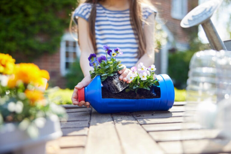 Young girl planting flowers in recycled blue container.