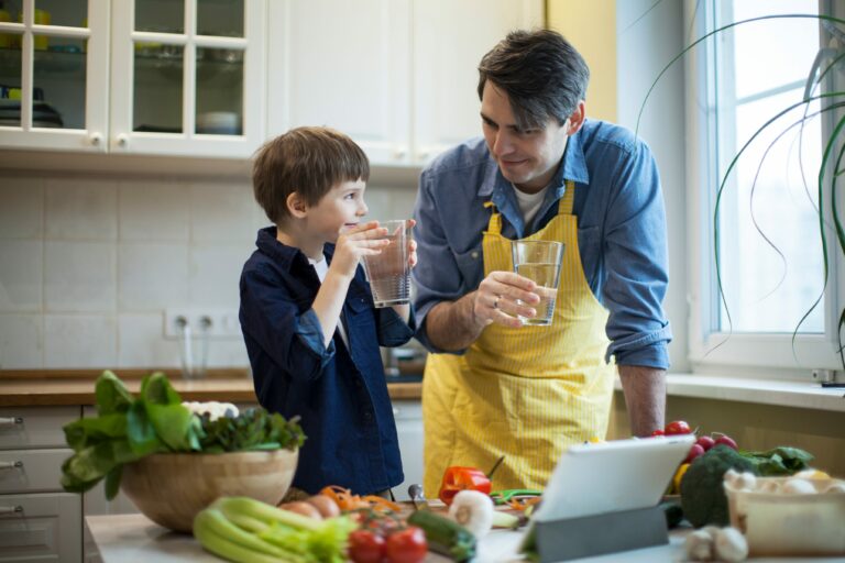Father and son drinking a glass of water in kitchen while cooking