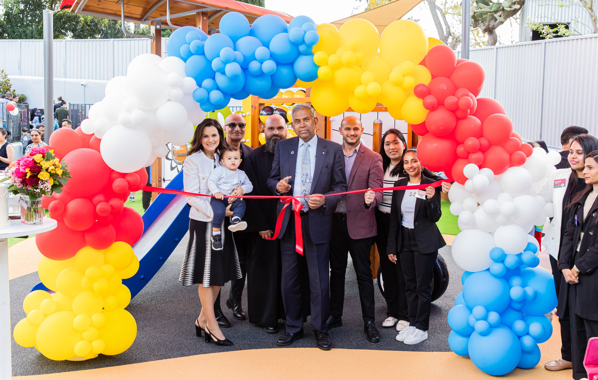 Balloon arch with guests standing behind red ribbon