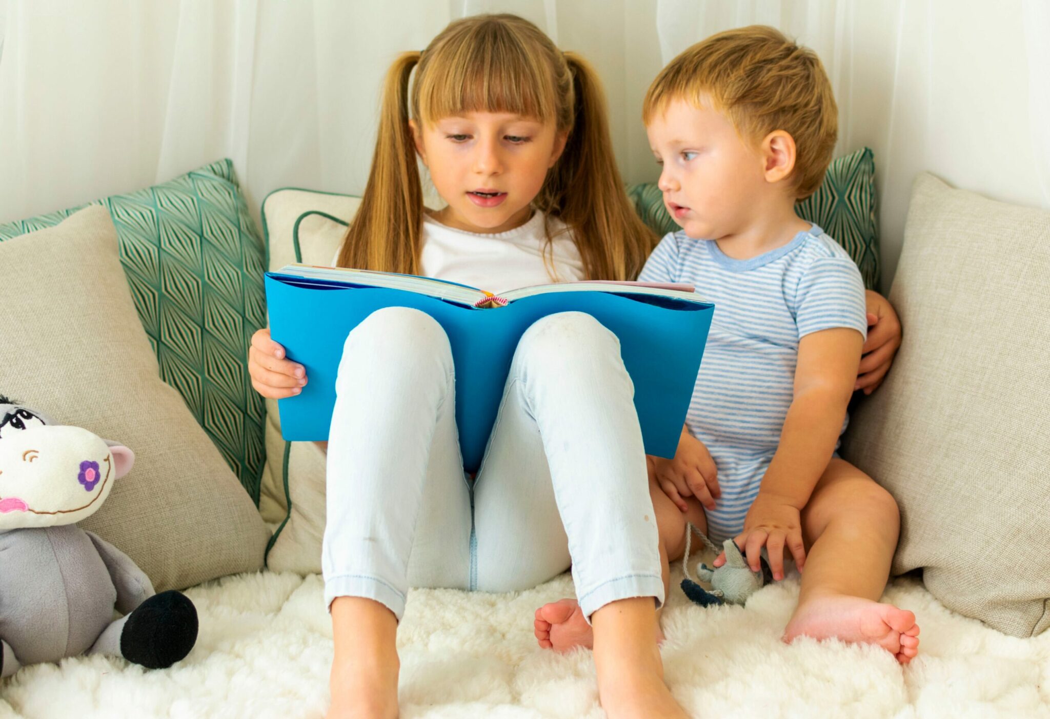 Young girl reading a book to younger boy in cosy corner
