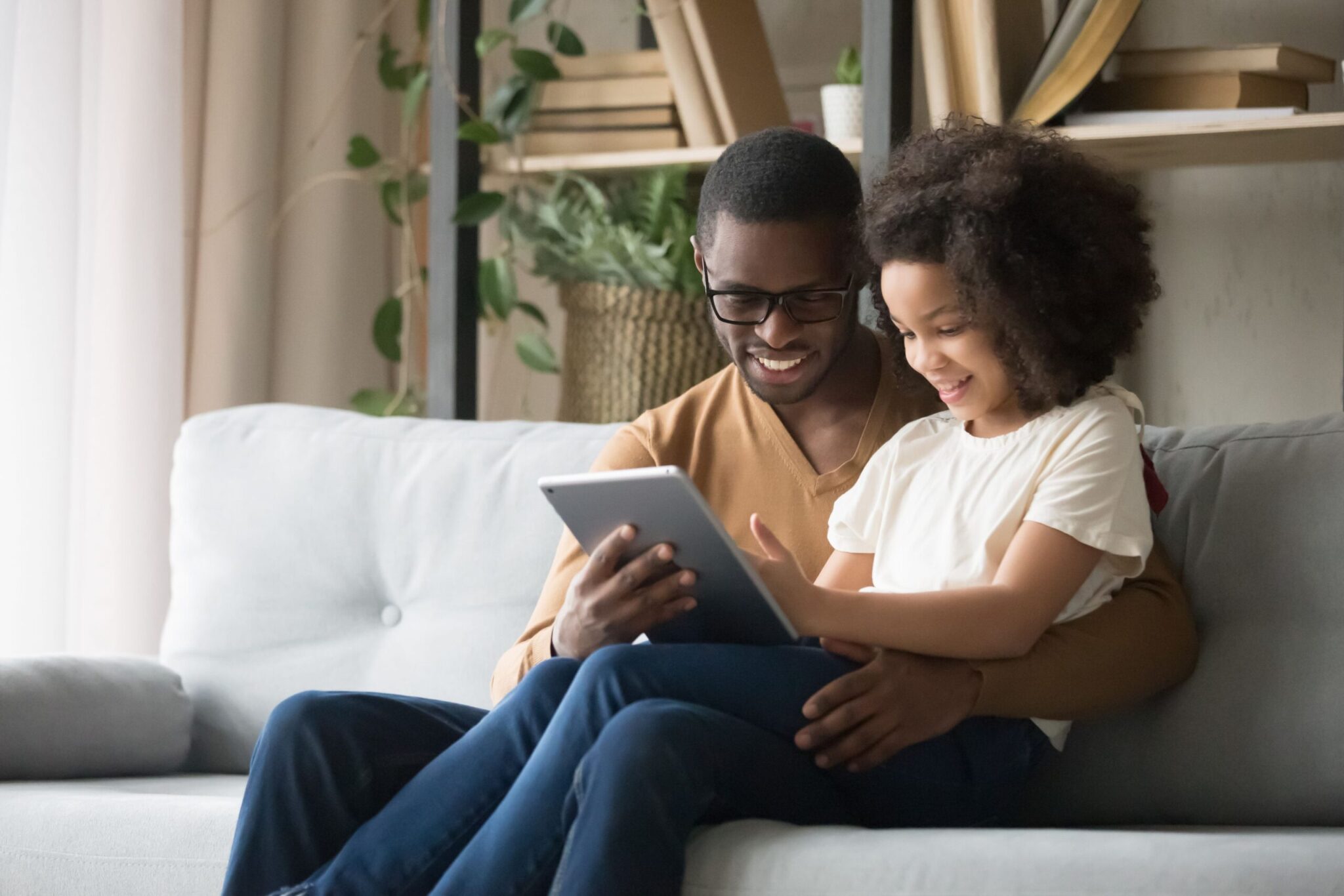 A child sitting on father's lap looking at a tablet