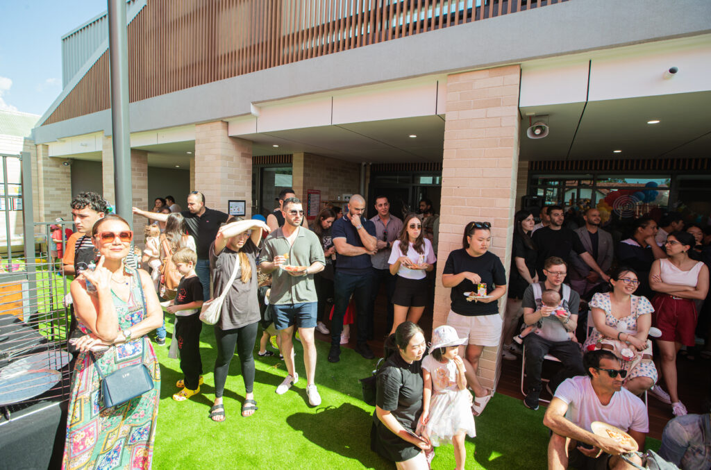 A crowd of young families gathers in the outdoor playground at Panania Montessori Academy to enjoy the grand opening speeches and witness the official ribbon-cutting ceremony.