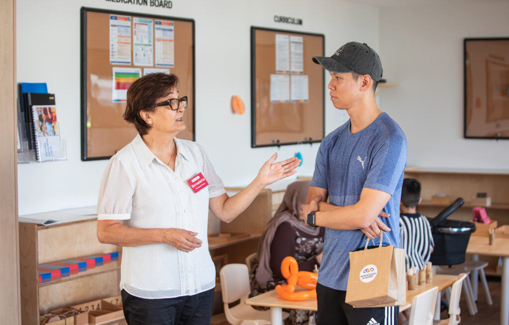 A qualified Montessori trainer speaks with a young dad, explaining the benefits of the Montessori preschool program and how it supports each child’s individual development and love of learning.