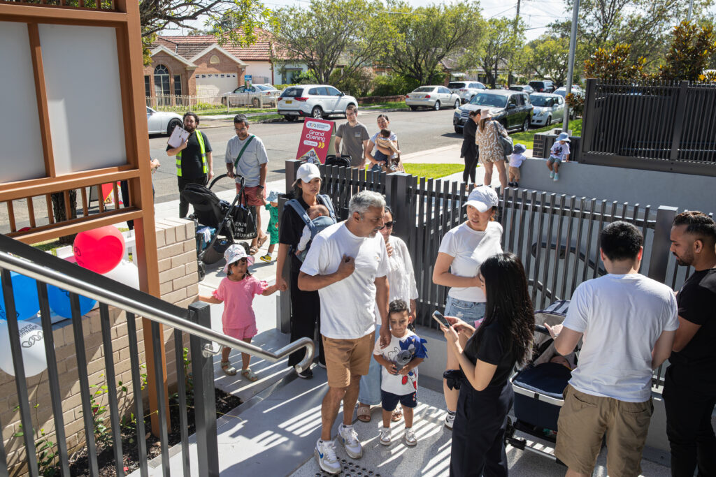 A crowd of young families gathers at the main entry of Panania Montessori Academy, eagerly awaiting the start of the grand opening event.