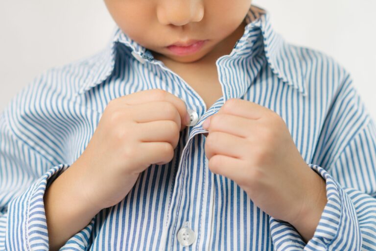 Young boy buttoning blue and white striped shirt