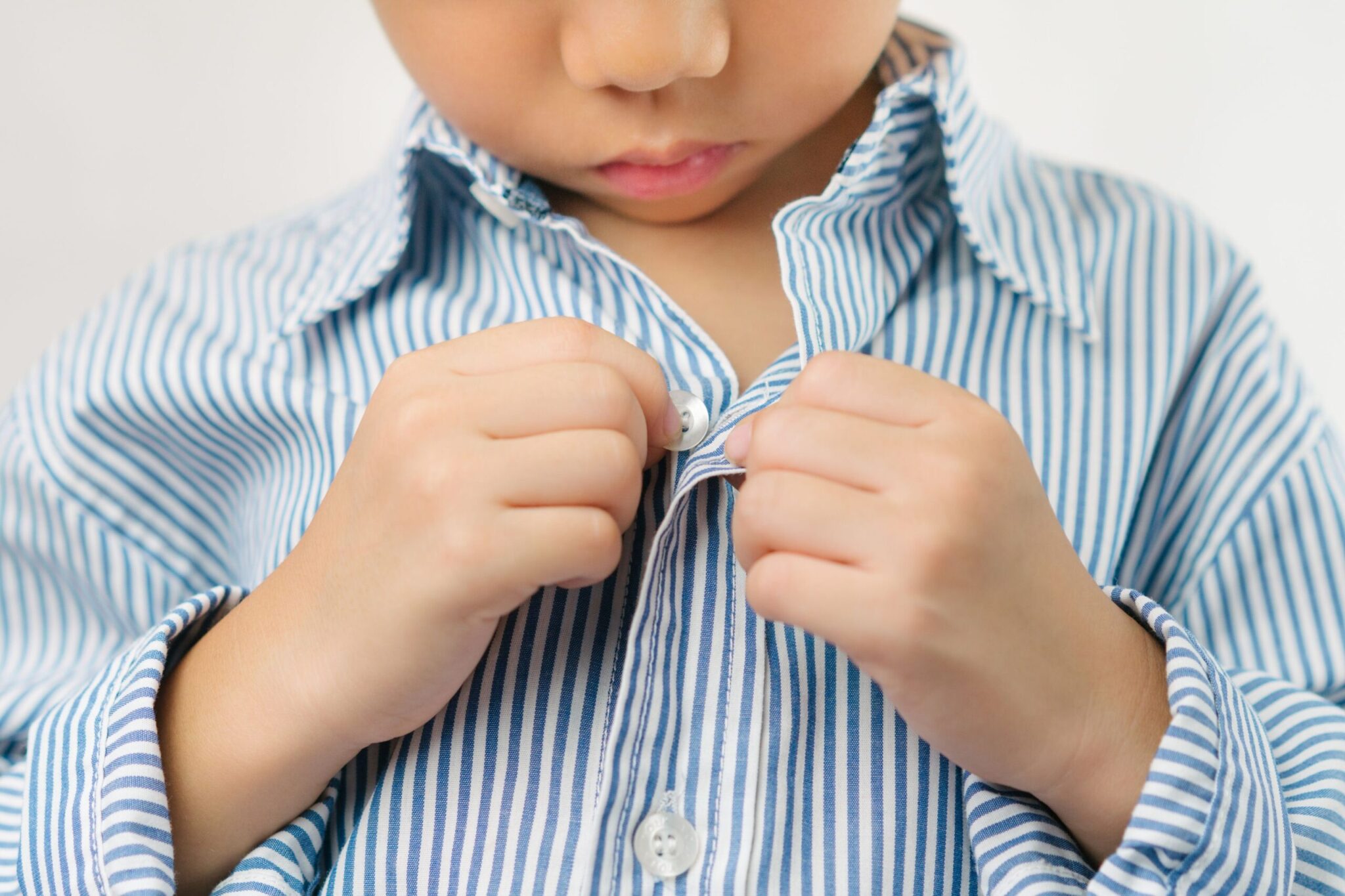Young boy buttoning blue and white striped shirt