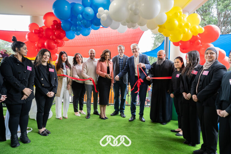 Councillors and VIP guests smile as they cut a ribbon tied to a colourful balloon arch, celebrating the grand opening of a childcare centre.