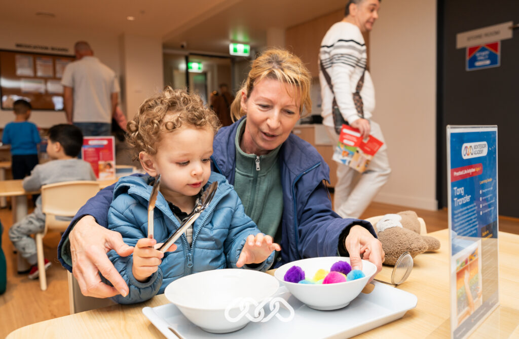 Child and parent enjoys Montessori practical life tong transfer activity at Bexley grand opening event in toddler room.
